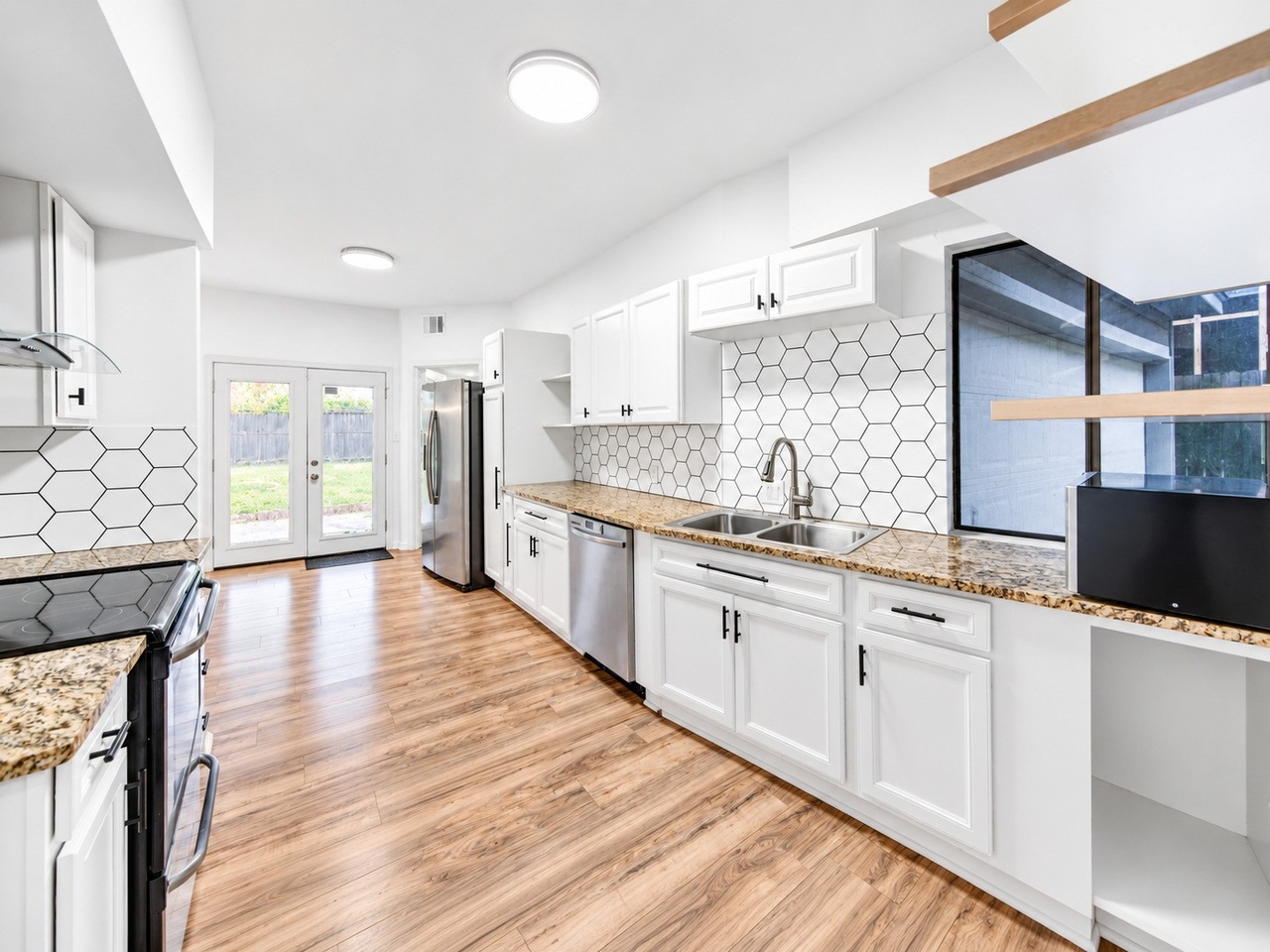 Bright white kitchen with granite counters and hex-tile backsplash